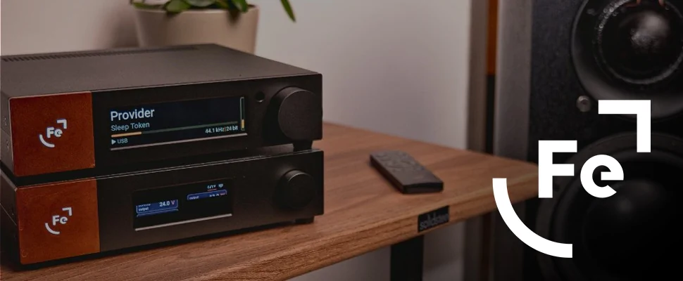 A sleek audio system with digital displays placed on a wooden shelf, accompanied by a remote and a speaker. Modern, technology-focused vibe.