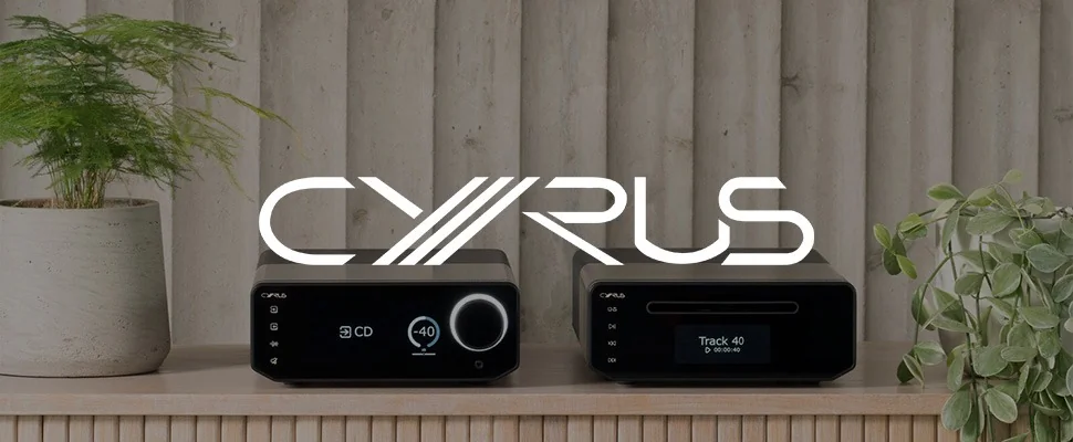 Two sleek black Cyrus audio devices are displayed on a wooden shelf with lush potted plants. The ambiance is modern and sophisticated.