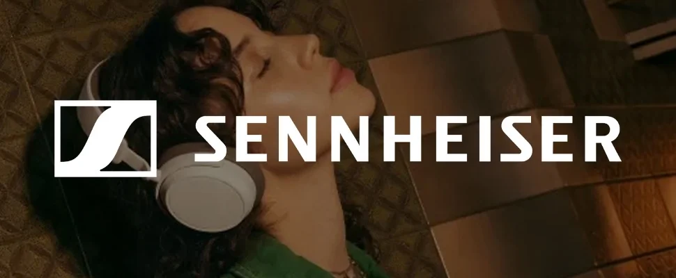Close-up of a person wearing grey Sennheiser headphones against a textured brown background. The Sennheiser logo and name appear on the right.