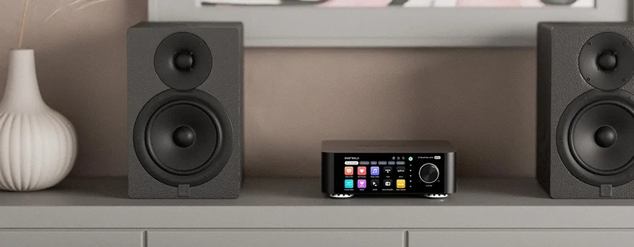 A sleek stereo system with a digital interface and vibrant display is flanked by two black speakers on a light grey shelf, with a modern vase nearby.