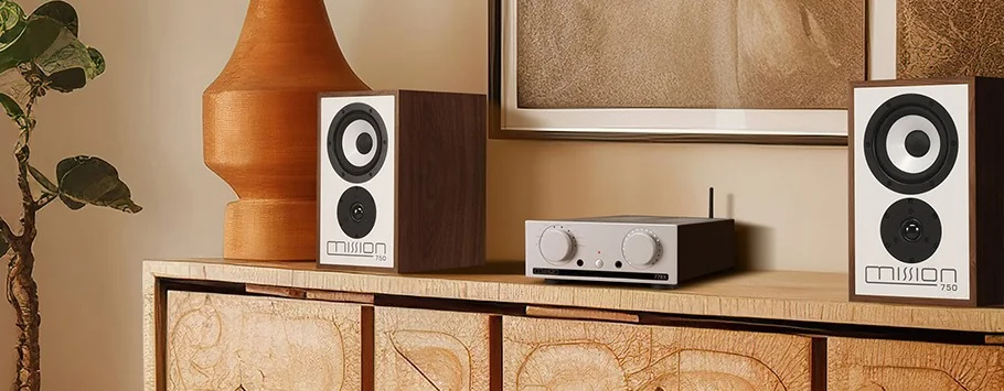 A stylish living room setup features two wooden speakers flanking a sleek amplifier on a textured wooden cabinet. A leafy plant and a large vase add warmth to the neutral tones, creating an inviting and modern ambience.