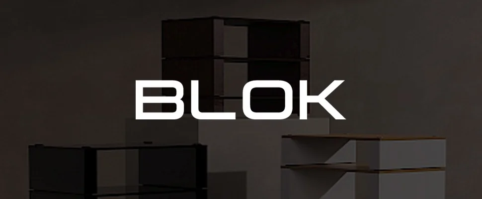 Minimalist room with geometric storage units in black and white on platforms, set against a grey wall. The word "BLOK" is visible.