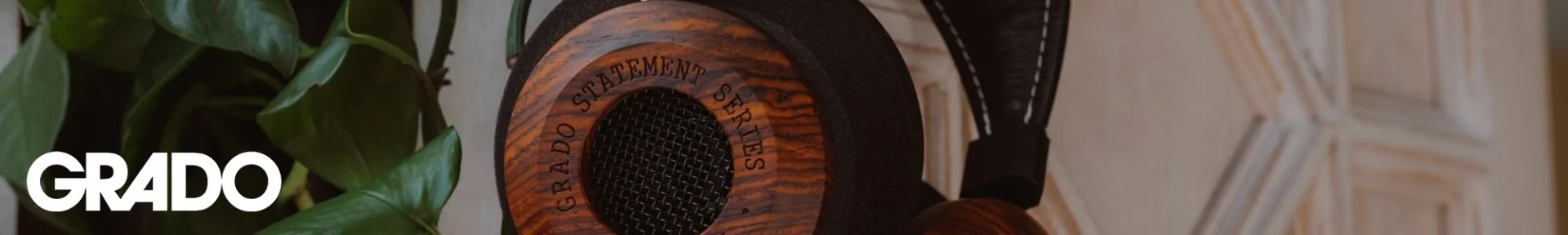 Close-up of a wooden-cased Grado headphone labeled "Statement Series," set against green leaves and a white textured background.