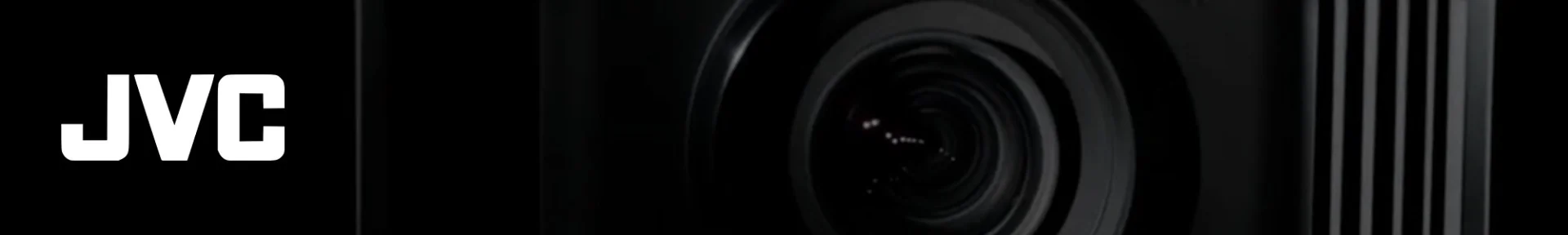 Close-up of a black camera lens on the right against a dark background. The bold white "JVC" logo appears on the left, creating a sleek, professional tone.