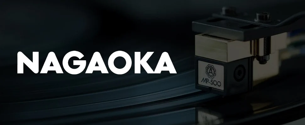 Close-up of a Nagaoka MP-500 cartridge playing a vinyl record, with the brand name "NAGAOKA" in bold white text on the left. The scene conveys precision and high-quality audio.