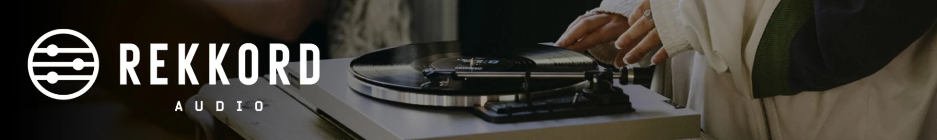 Close-up of a vinyl record being placed on a turntable. The background features the logo and text 'REKKORD AUDIO.' The scene conveys a sense of vintage nostalgia and music appreciation.