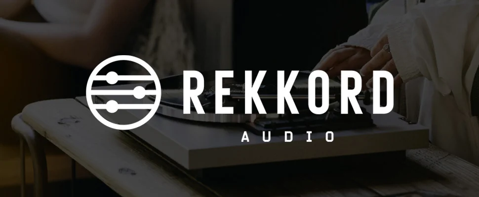 Close-up of a vinyl record being placed on a turntable. The background features the logo and text 'REKKORD AUDIO.' The scene conveys a sense of vintage nostalgia and music appreciation.