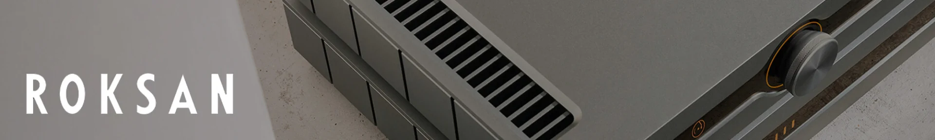 Close-up of a sleek, modern audio amplifier with a metallic surface and air vents, next to the stylized white text 'Roksan' on a grey background