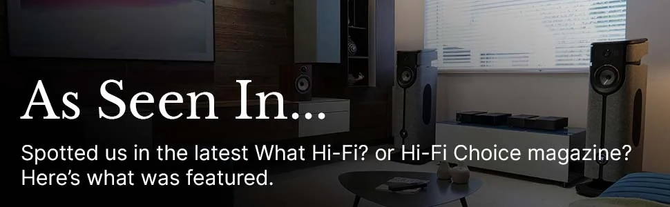 Living room featuring large speakers, modern d&eacute;cor, and a coffee table. Overlay text reads, "As Seen In... What Hi-Fi? or Hi-Fi Choice magazine?"