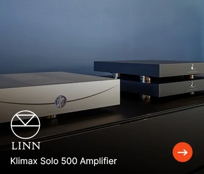 Two sleek black Linn Klimax Solo 500 amplifiers on a dark surface, set against a dark blue wall. The mood is modern and sophisticated.