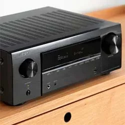Black audio receiver with control knobs and display panel, placed on a wooden surface.