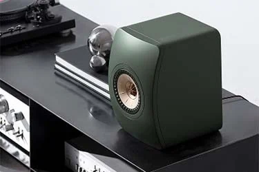 Stylish green speaker on a black shelf, next to a turntable and audio equipment, embodying modern audio design.