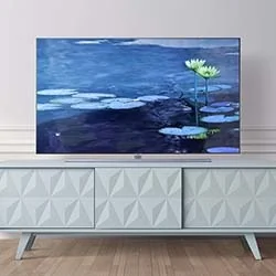 A modern television displaying Monet's water lilies sits atop a light blue, textured media console against a white wall.