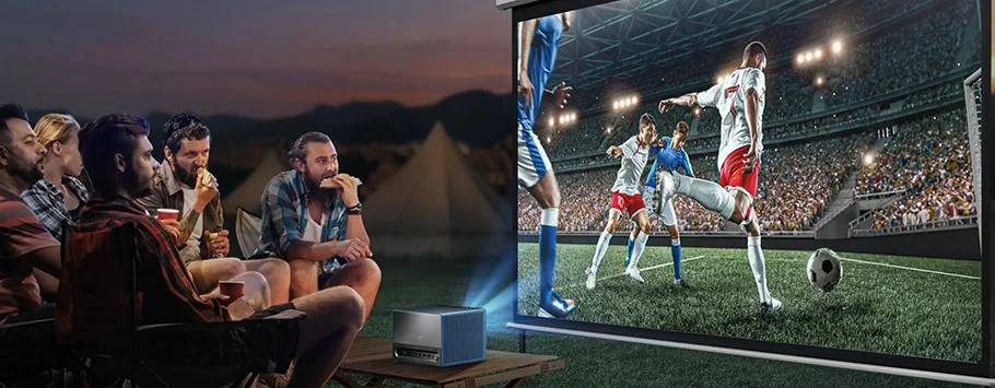 A group of people sitting outdoors, focused on a projected soccer match. The screen shows players mid-action in a stadium, creating an engaging and lively atmosphere.