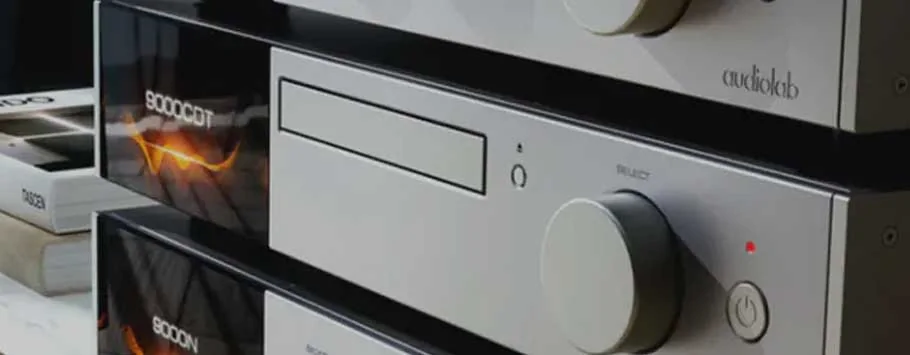 A sleek black audio CD player sits atop a wooden cabinet with a modern, minimalist design. Soft lighting casts gentle shadows.