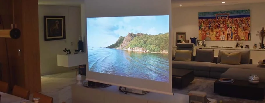 A serene coastal scene is projected onto a screen in a cosy living room, featuring a large sofa, vibrant artwork, and ambient lighting.