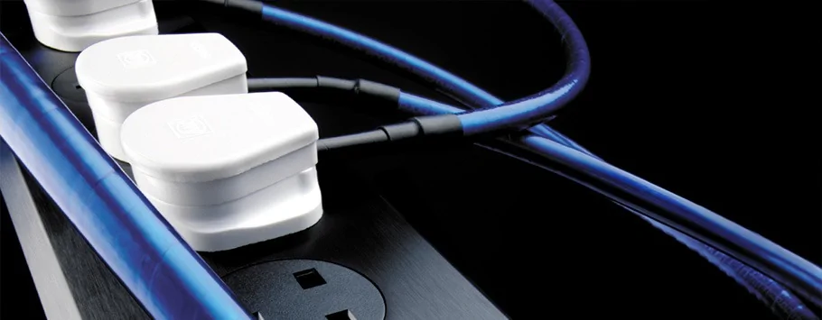 Close-up of white electrical plugs connected to a black power strip with blue cables, set against a dark background.