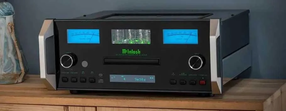 A sleek black audio CD player sits atop a wooden cabinet with a modern, minimalist design. Soft lighting casts gentle shadows.
