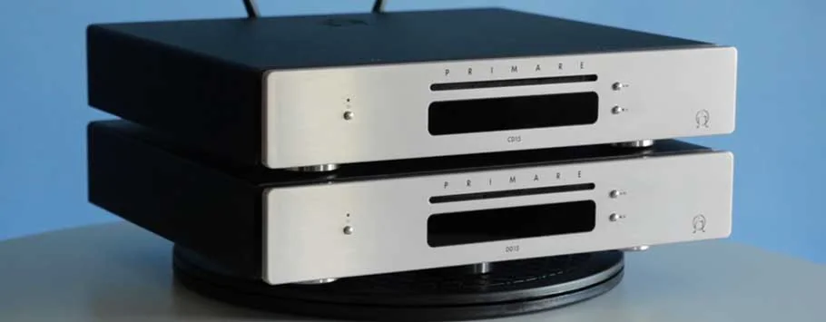A sleek black audio CD player sits atop a wooden cabinet with a modern, minimalist design. Soft lighting casts gentle shadows.