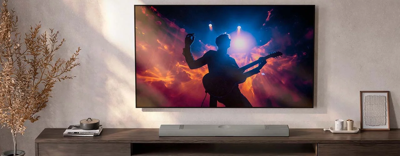 A modern living room with a wall-mounted TV displaying a vibrant silhouette of a guitarist against fiery lights. Nearby, a sleek soundbar and minimalist d&eacute;cor.