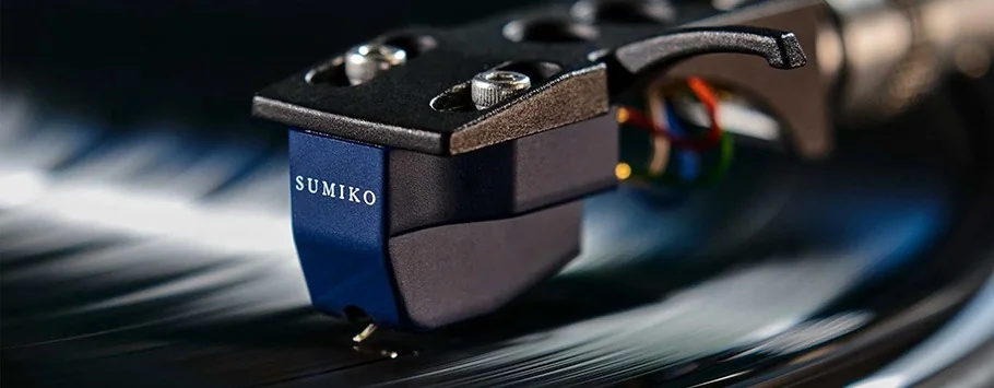 Close-up of a Sumiko phono cartridge gliding over a vinyl record, highlighting precision and nostalgia with a sleek, modern design against a blurred background.
