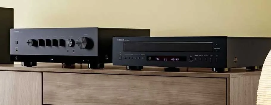 A sleek black audio CD player sits atop a wooden cabinet with a modern, minimalist design. Soft lighting casts gentle shadows.
