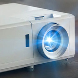 A bright projector emits a focused blue light from its lens, set on a smooth surface. The white casing conveys a sleek, modern design.