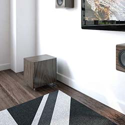 Modern living room corner with a hardwood floor, geometric black and white rug, wall-mounted speakers, and a TV. The ambiance is sleek and minimalistic.