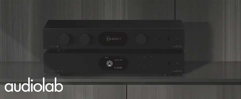 A sleek, modern audio system on a wooden shelf. The black design features two stacked units with controls and digital displays. 'Audiolab' logo is visible, conveying a high-tech and minimalist aesthetic.