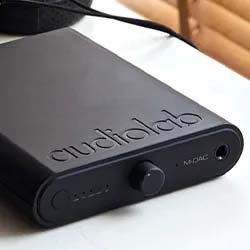 Sleek black audiolab M-DAC with a smooth finish, set on a white surface. The device features a central knob and conveys a modern, minimalist design.