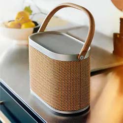 Stylish portable speaker with a woven texture and leather handle on a countertop. In the background, a bowl of lemons adds a touch of color.