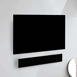 A minimalistic room with a flat-screen TV and soundbar mounted on a white wall. The corner of a round mirror is visible in the bottom right.