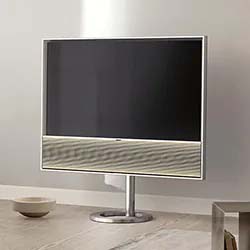 Sleek, modern television with a thin metallic frame and pedestal stand, set in a minimalist room with light walls and neutral-toned decor.