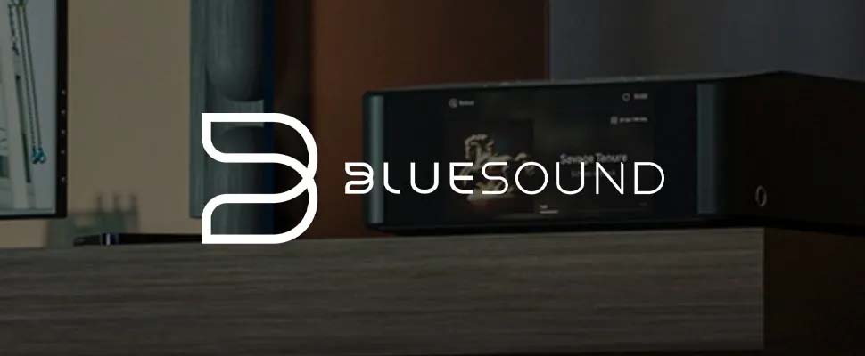 Bluesound logo overlaying a sleek audio system on a wooden shelf. The setting is modern and minimalistic, conveying a sense of high-tech sophistication.
