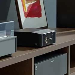 A sleek black audio device sits on a modern brown shelf, next to abstract art with red and yellow hues. The setting is neat and contemporary.