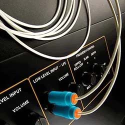 Close-up of an audio system showing connected cables in low-level input jacks, black volume knobs, and labeled frequency control switches, conveying a techy vibe.