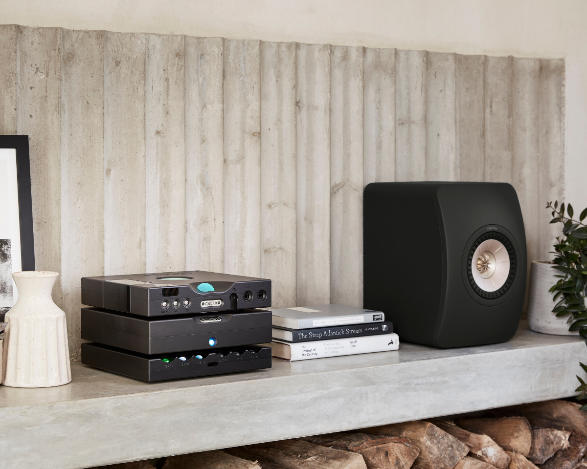 A sleek audio setup on a concrete shelf features stacked black audio components with glowing lights, a modern speaker, books, and a ceramic vase, creating a minimalist and sophisticated tone.