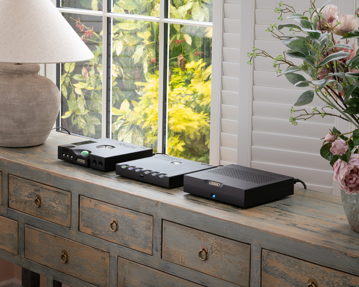A rustic wooden console with electronic devices, a stone lamp, and a vase of pink flowers. Sunlight filters through the window, casting a cozy glow.