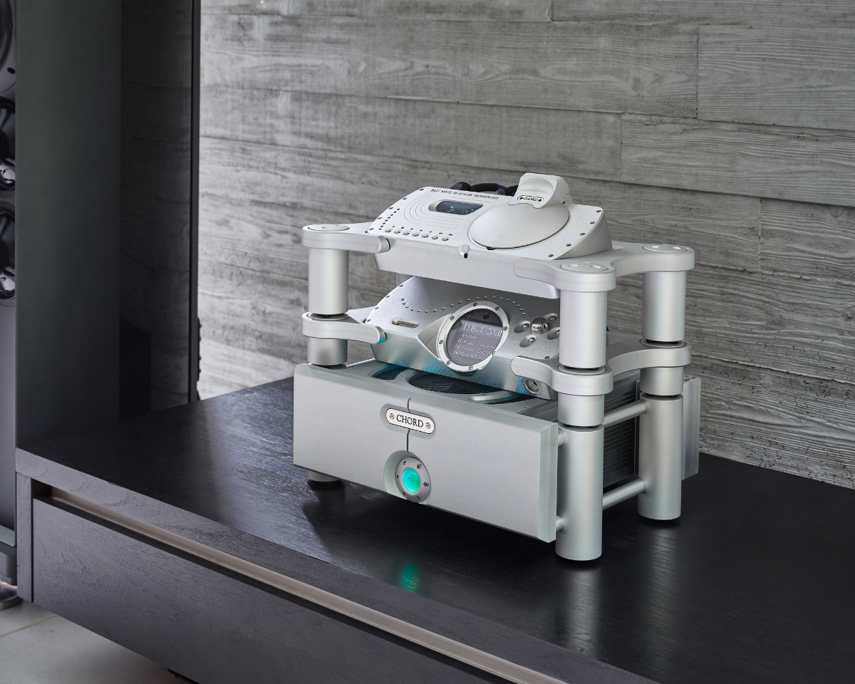 A sleek, silver audio setup with futuristic design features stacked components on a dark wooden table. The setting is modern and minimalist.