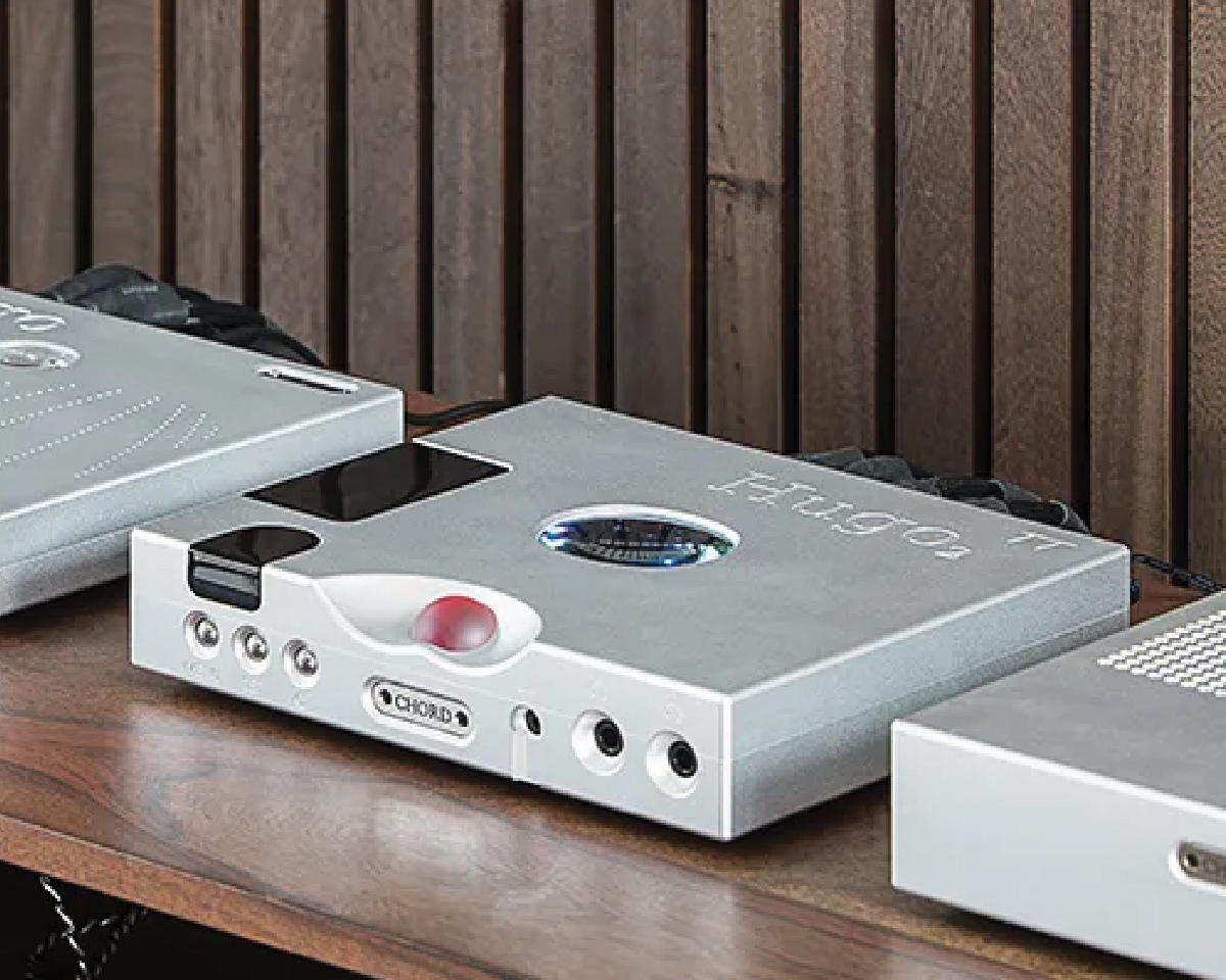 Silver audio equipment sits on a wooden shelf, featuring modern design with glowing buttons and circular accents, conveying a sleek, high-tech aesthetic.