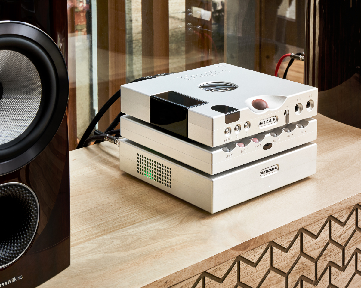 A sleek audio setup on a wooden table features stacked silver amplifiers with intricate controls, next to a large speaker, conveying a modern and sophisticated vibe.