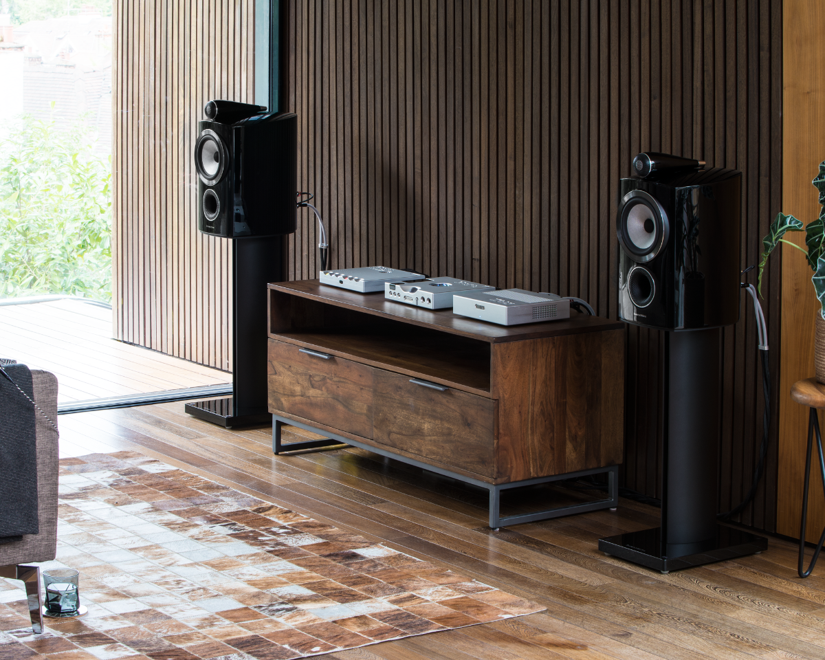 Modern living room with a wooden media console holding audio equipment, flanked by sleek black speakers. The space has a warm, cozy vibe.