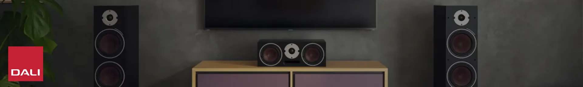 Modern living room setup featuring a large speaker and a smaller speaker on a cabinet. A red square DALI logo is centered over the image. Sleek and minimalist.