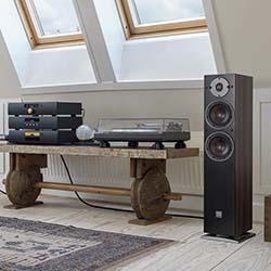 A cozy attic room with natural light features a stylish wooden bench holding a vinyl record player and audio system, flanked by a sleek black speaker.