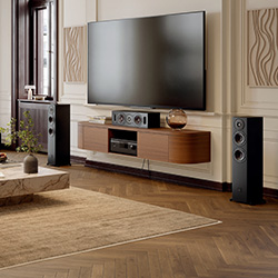 A modern living room with a large flat-screen TV, brown sectional sofa, elegant wood floor, marble coffee table, and tall speakers, creating a cozy ambiance.