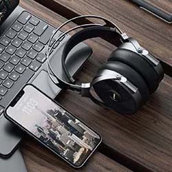 A sleek smartphone displaying a cityscape is placed next to a laptop and stylish over-ear headphones on a wooden desk, creating a modern, tech-savvy vibe.