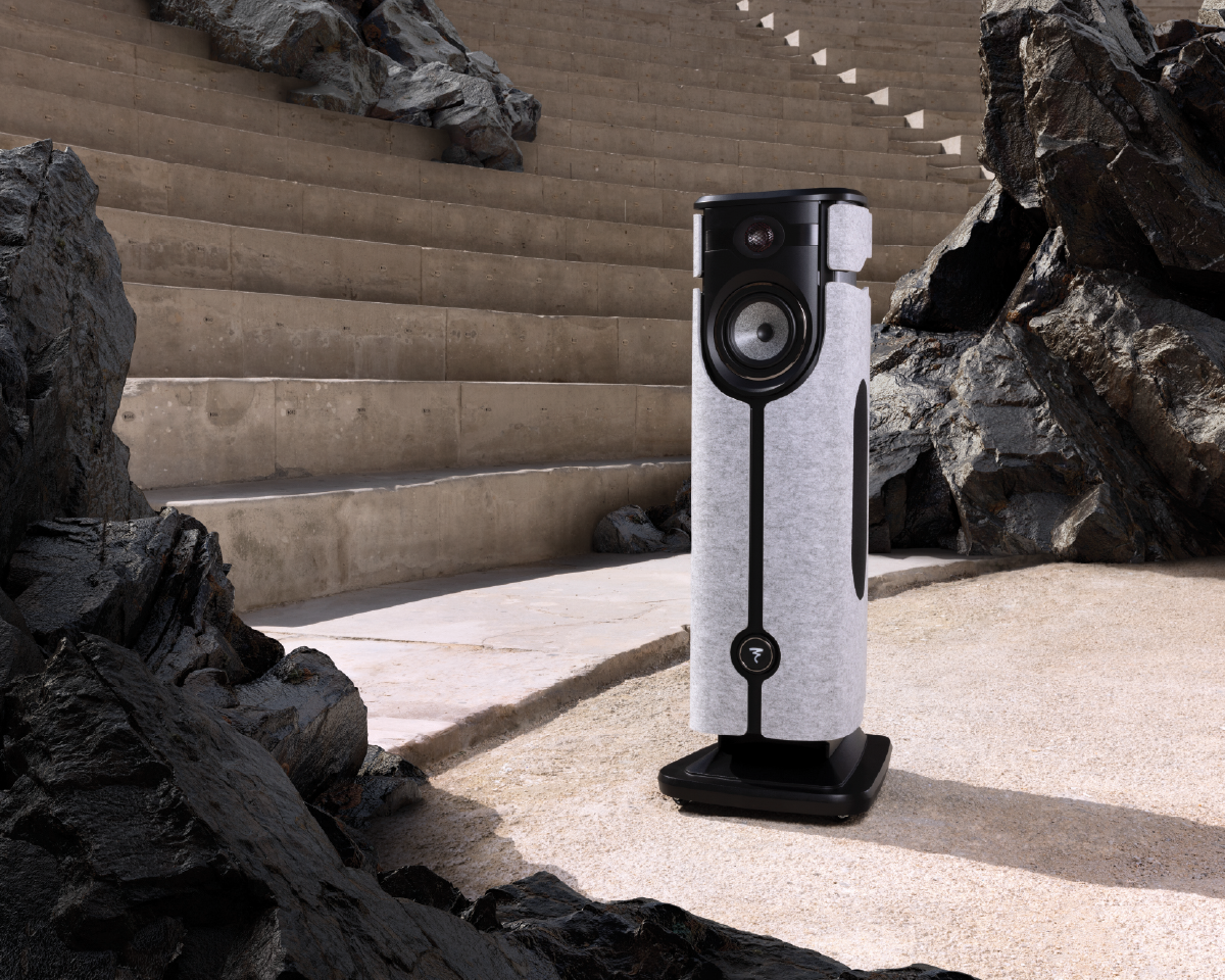 A sleek, modern speaker with a textured finish is positioned outdoors, surrounded by rugged rocks and concrete steps, reflecting a blend of nature and technology.
