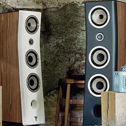 Two sleek tower speakers, one white and one black, stand indoors against a textured wall. The scene conveys a modern and stylish audio setup.