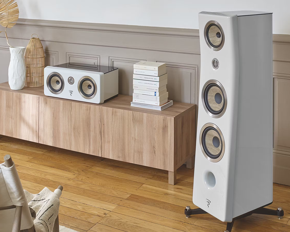 Modern living room with tall, white hi-fi speakers and a matching smaller speaker on a wooden console. Stack of books and decor add a cozy touch.
