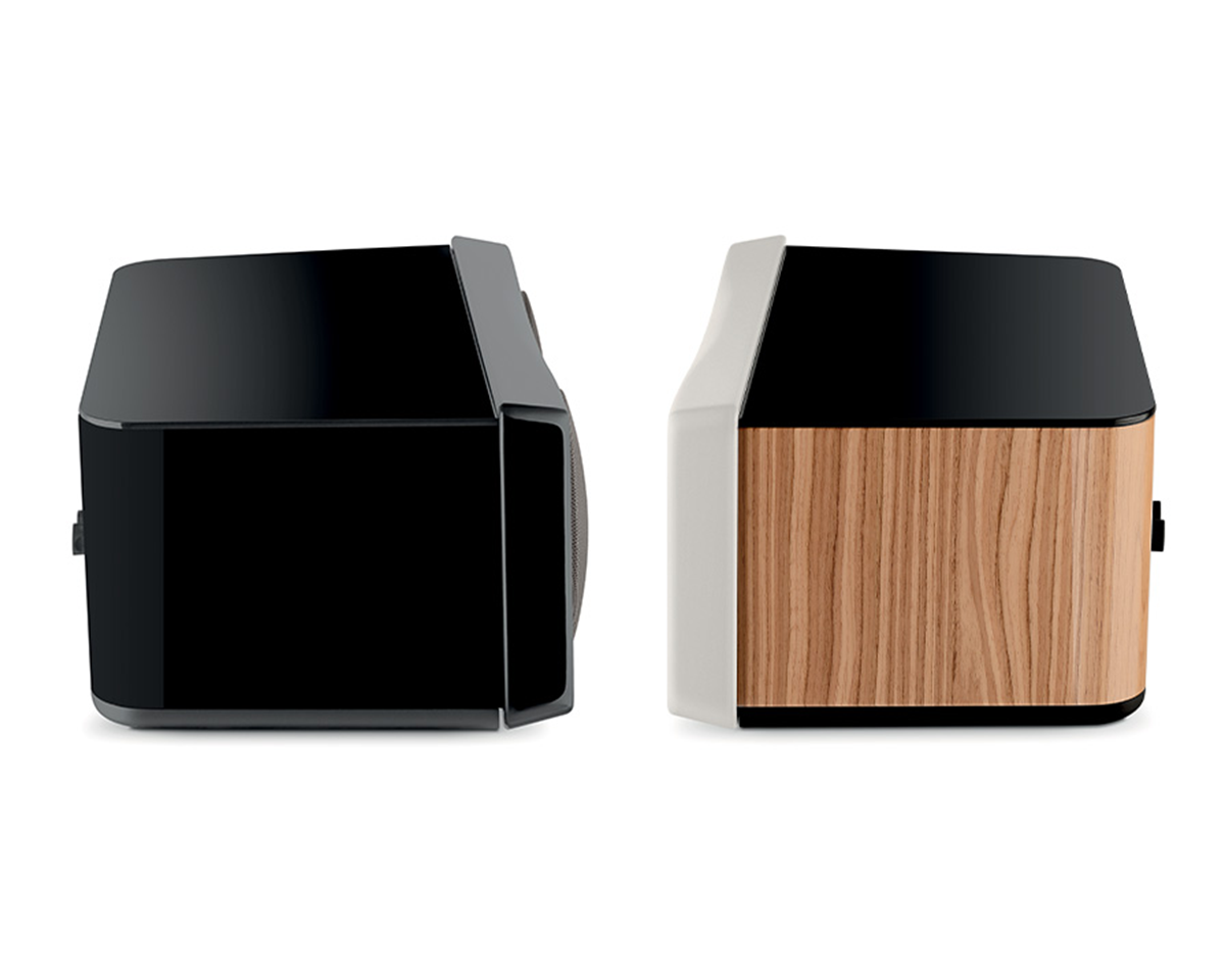 Two modern speakers side by side, one black with a sleek finish and the other featuring a light wood panel. Both have a minimalist, angular design.